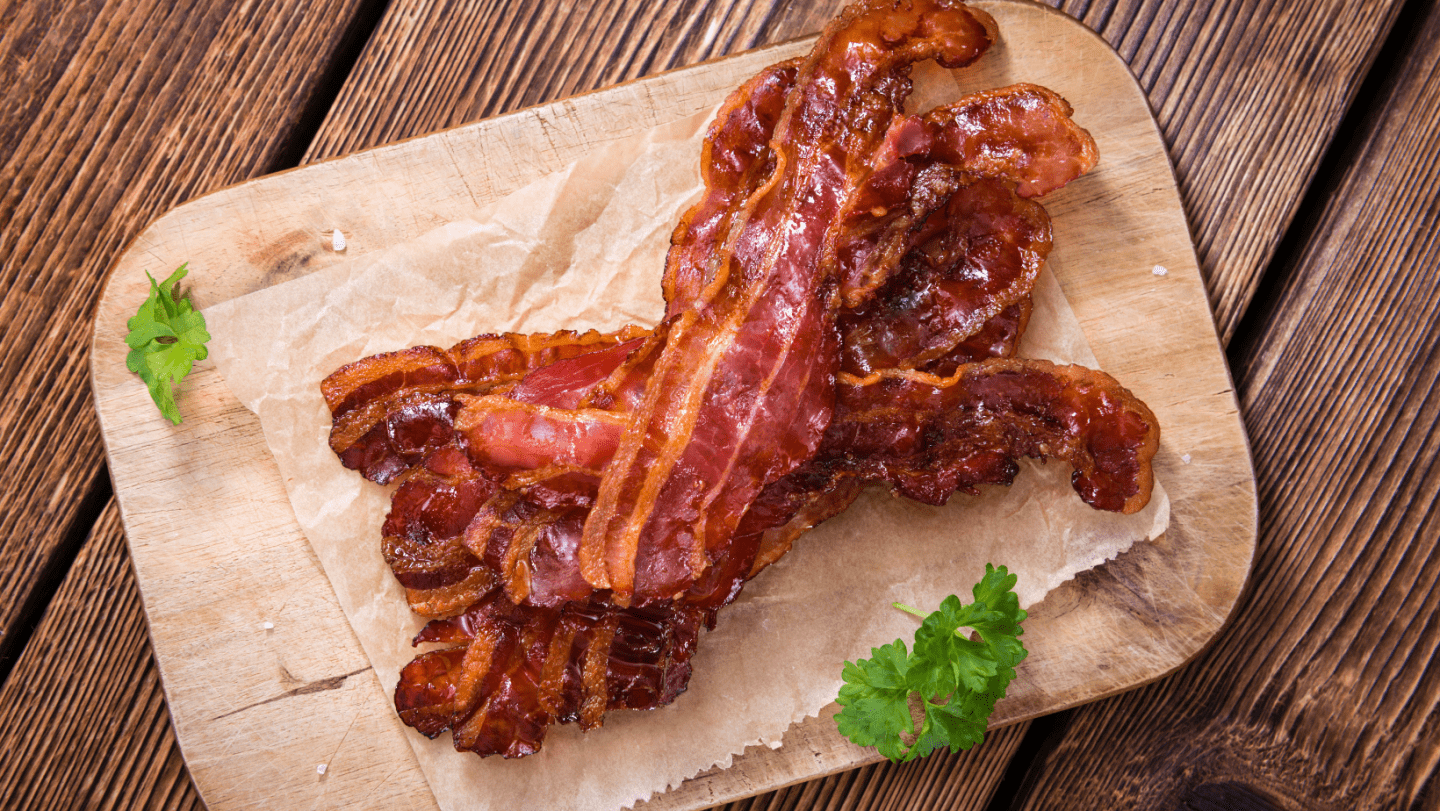 how to cook bacon in the oven - bacon on a piece of parchment paper on a wooden cutting board