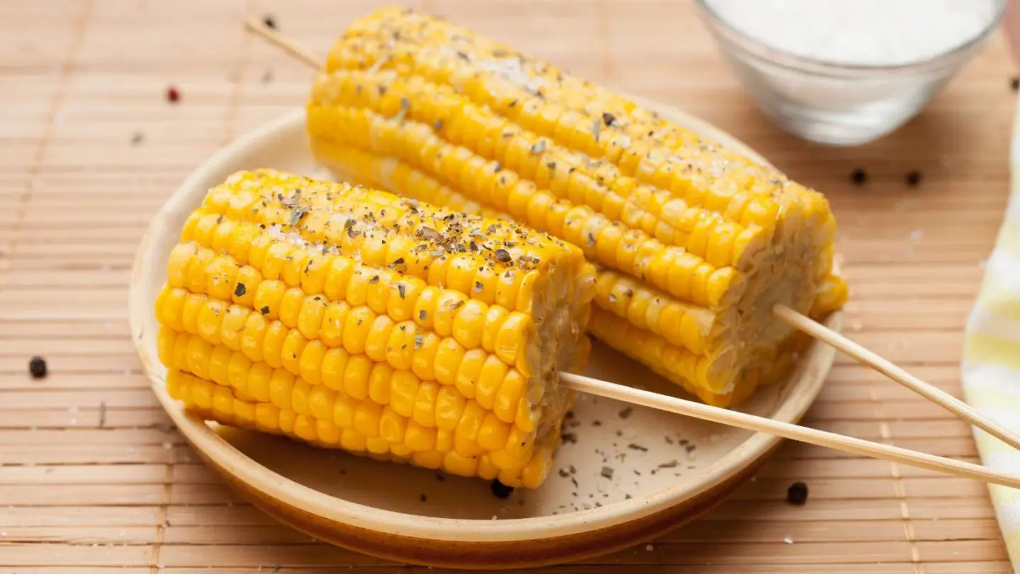 how to boil corn on the cob - skewered corn that is seasoned on a plate