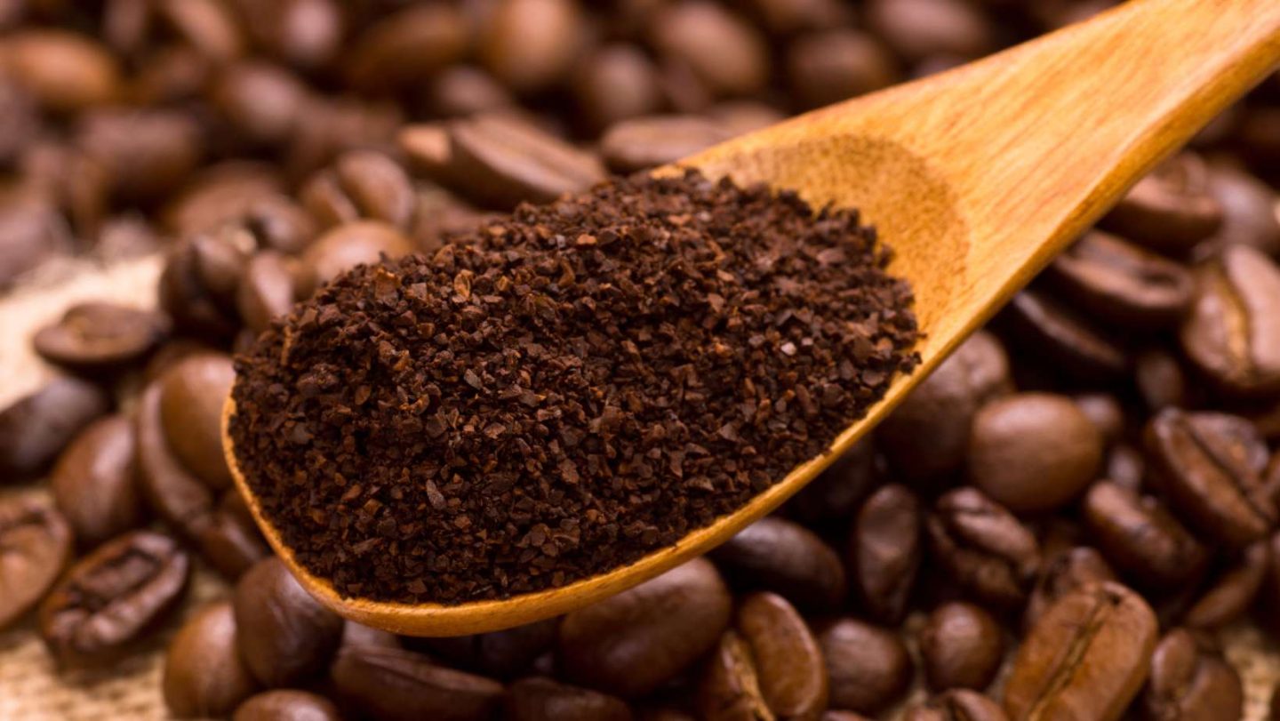 do coffee grounds attract rats - wooden spoon of coffee grounds held above a pile of coffee beans