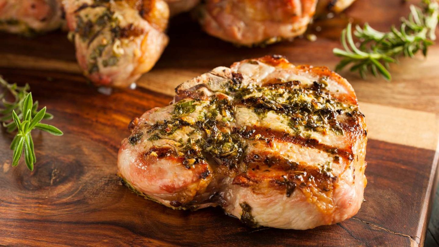 Pork Cutlet vs Pork Chop - grilled pork chop with seasoning on top and sprigs of thyme placed around it on a wooden cutting board