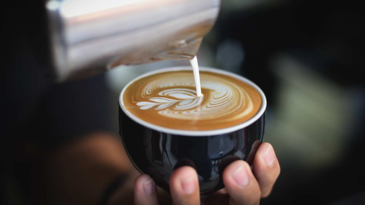 moka pot vs espresso - someon pouring cream into a latte creating latte art