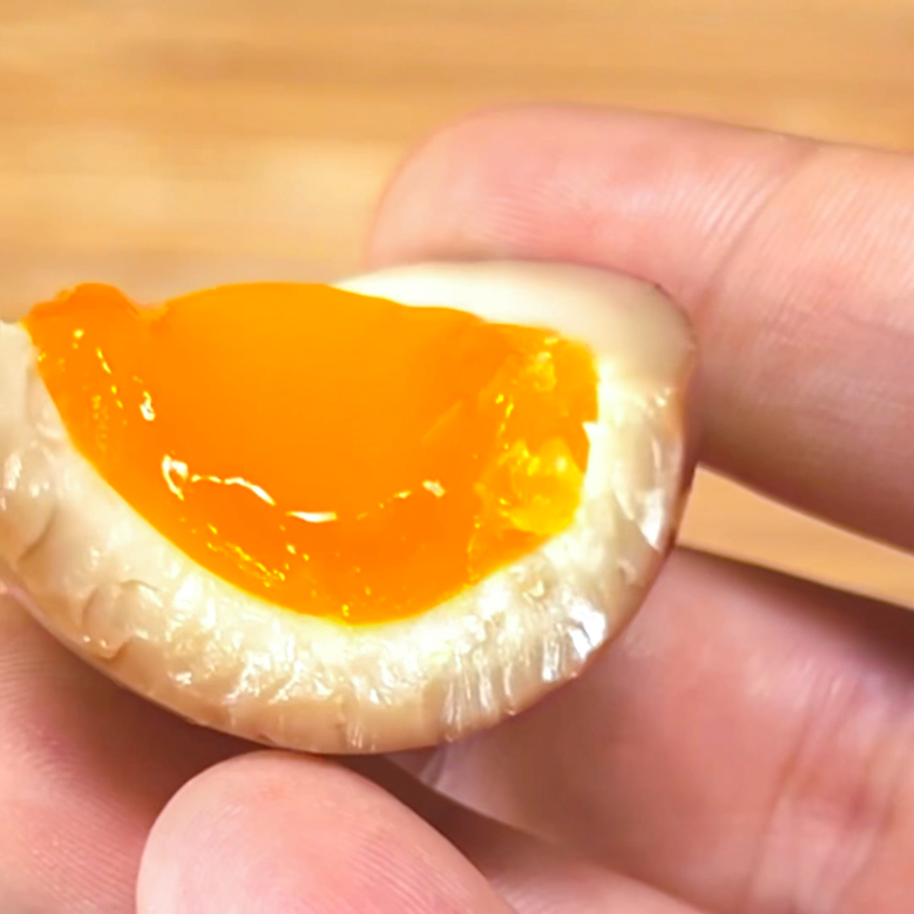 ramen egg recipe - holding a half of a ramen egg after taking a bite to see the cross section of the white and yolk